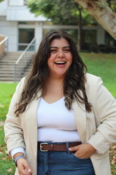 Fernanda Rojas wearing a tan blazer and jeans standing outdoors smiling  