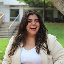 Fernanda Rojas wearing a tan blazer and jeans standing outdoors smiling  