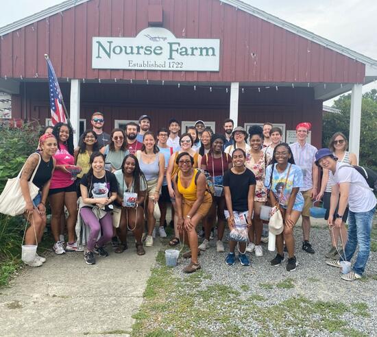 Twenty or so people pose outside of a red farmhouse style building